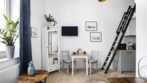 A compact living space with a dining area, a TV mounted on the wall, a ladder leading to a kitchen, and a potted plant.