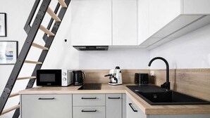 A modern kitchen with a microwave, coffee maker, and kettle on the countertop, a black sink, and a wooden ladder against the wall.