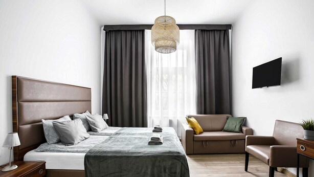 Ett modernt hotellrum med en stor säng, en soffa, en fåtölj, en TV och ett fönster med gardiner.