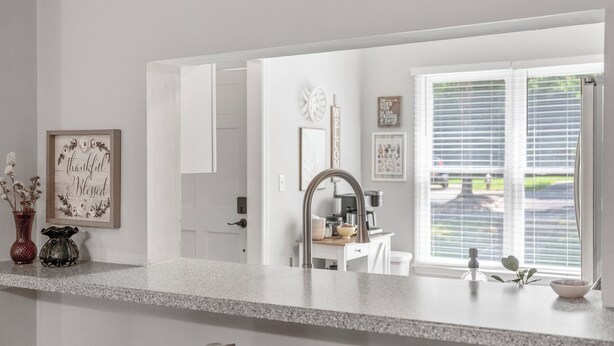 A modern kitchen with a granite countertop, a stainless steel faucet, and a view through a window with blinds.