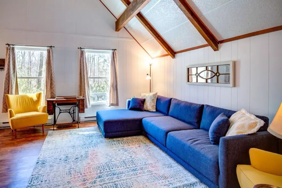 A cozy living room with a sectional sofa, a yellow armchair, a sewing machine, and a patterned rug.