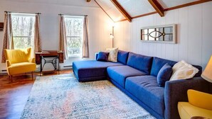 Een gezellige woonkamer met een hoekbank, een gele fauteuil, een naaimachine en een kamerbreed tapijt met een patroon.
