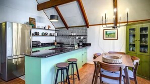 Een keuken met een centraal eiland, barstoelen, een eettafel met stoelen, een kroonluchter en een groen kastje met glazen deuren.