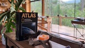 A wooden table with a book titled 'Atlas National Geographic', a candle, and a decorative piece. - YAAHOO ECOLODGE (Bocaina do Sul)