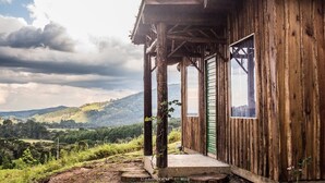 A rustic wooden cabin with a porch, a window, and a view of a mountainous landscape. - YAAHOO ECOLODGE (Bocaina do Sul)