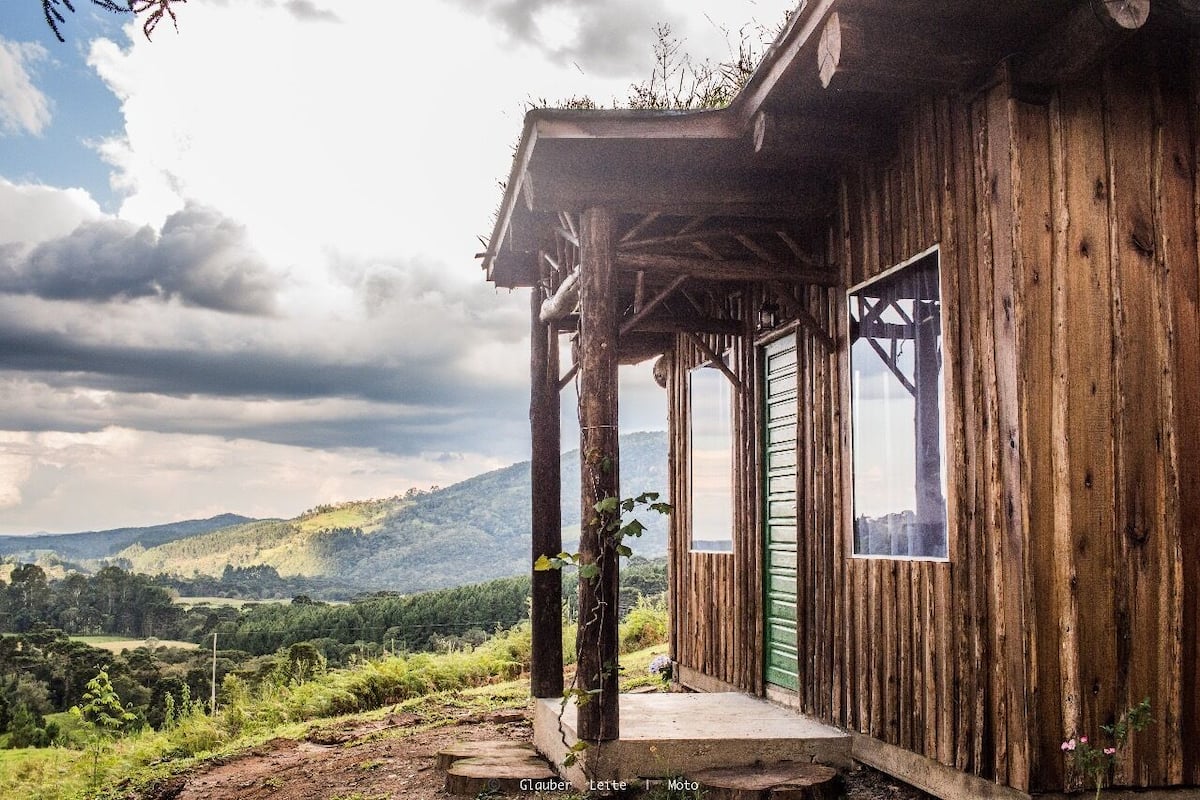 Una cabaña de madera rústica con un porche, una ventana y vistas a un paisaje montañoso.