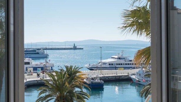 A marina with boats, a palm tree, and a clear sky. - Apartment & Studio Riva Lucija by Litto (Split)