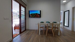 Un coin repas avec une table et des chaises, un téléviseur fixé au mur et une porte donnant sur un balcon.