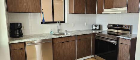A modern kitchen with wooden cabinets, a built-in dishwasher, a coffee maker, a toaster, and a stainless steel oven.