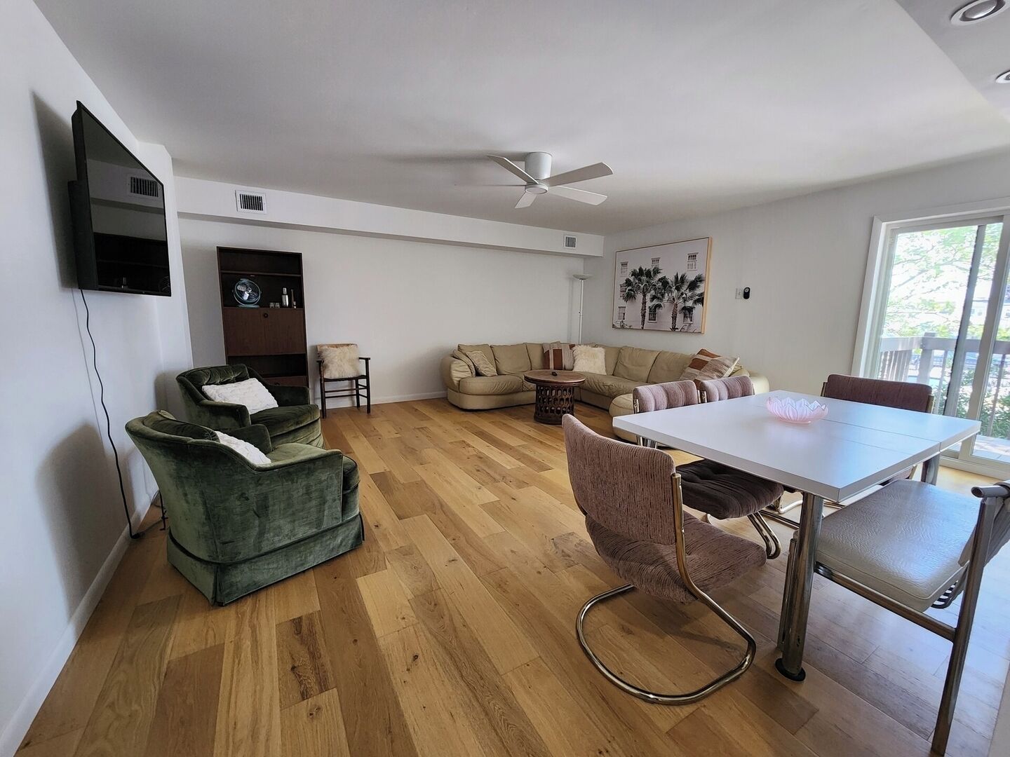 Een moderne woonkamer met een houten vloer, een bank, een eettafel en een plafondventilator.