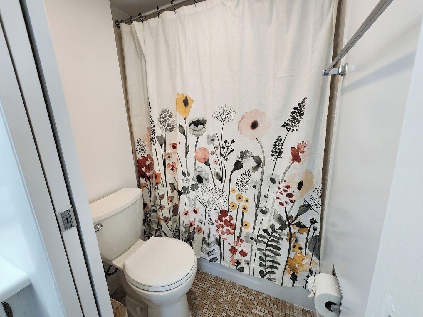 Un baño con inodoro, cortina de ducha estampada con motivos florales y dispensador de papel higiénico.