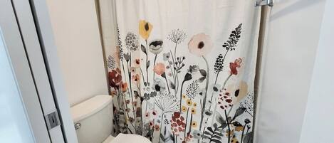 Un baño con inodoro, cortina de ducha estampada con motivos florales y dispensador de papel higiénico.