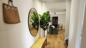 Un pasillo con un banco, un espejo, una cesta colgante y una planta.