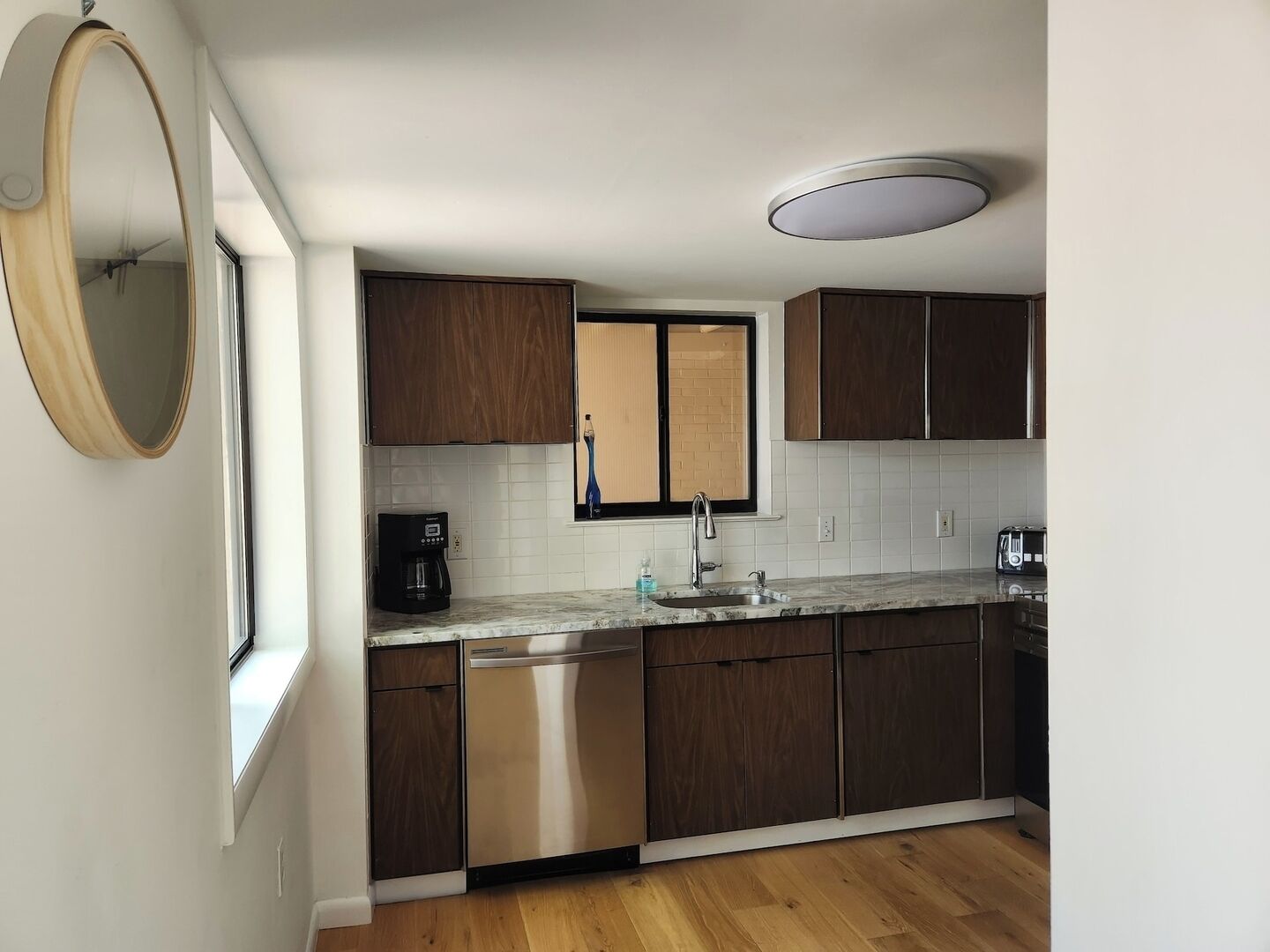 A modern kitchen with wooden cabinets, a stainless steel dishwasher, a coffee maker, and a window with a view.