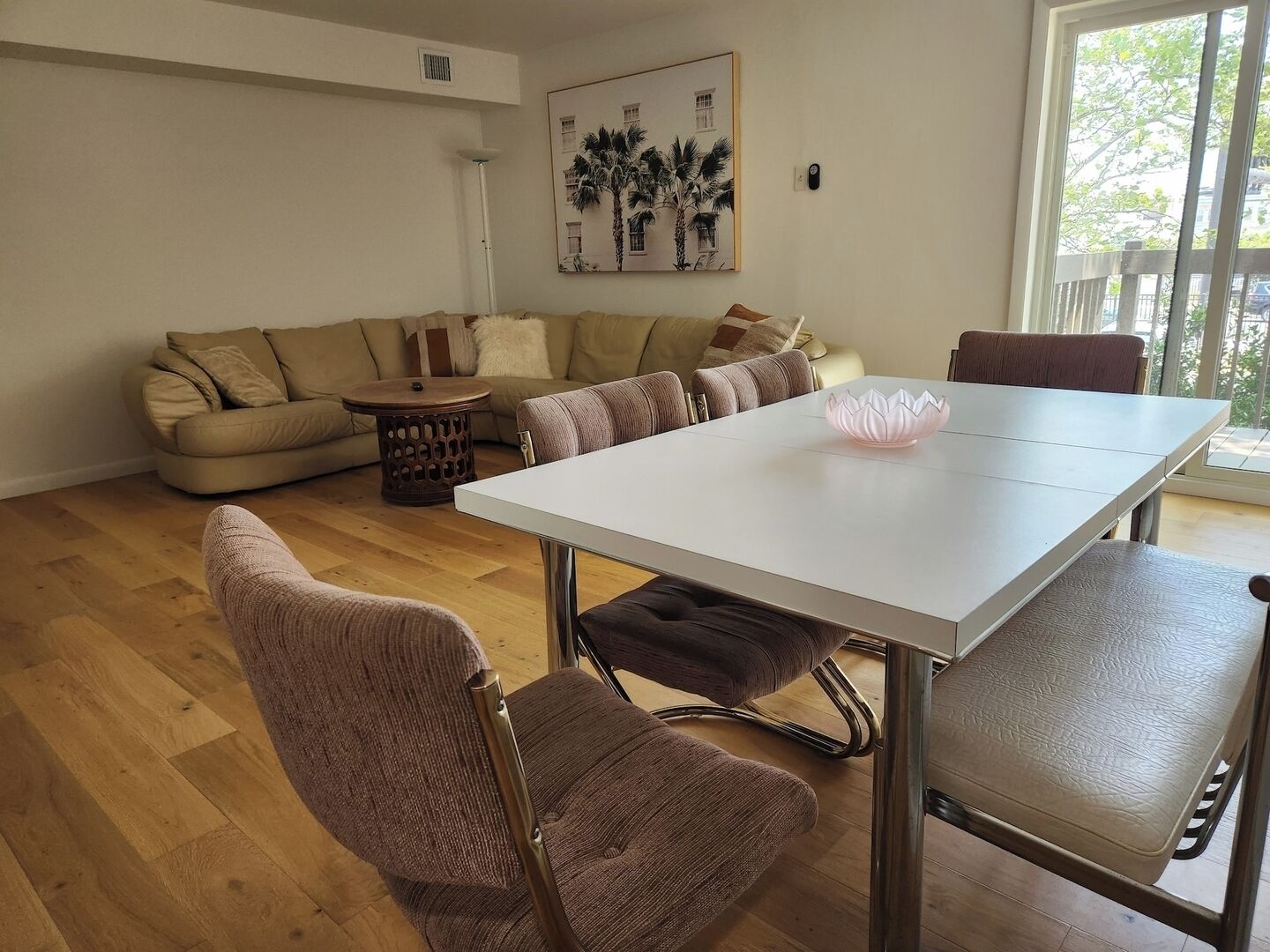 A living room with a white dining table, brown upholstered chairs, a beige sofa, and a small round side table.