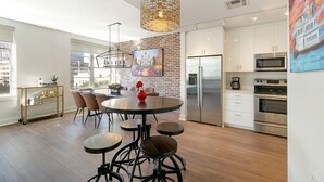 Una cocina moderna con pared de ladrillo decorativa, electrodomésticos de acero inoxidable y un comedor con mesa redonda y taburetes.