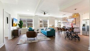 Amplia sala de estar con sofá azul, piso de madera y comedor con pared de ladrillo y muebles modernos.