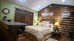 A rustic log cabin-style bedroom with a bed, two bedside lamps, a wooden dresser, a clock, and a framed picture on the wall. - The Lil House with Balcony (Robbinsville)