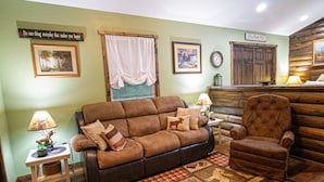 A cozy living room with a brown leather sofa, a matching armchair, a small side table with a lamp, and a patterned rug. - The Lil House with Balcony (Robbinsville)