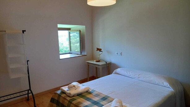A bedroom with a bed, a window, a desk, and a standing heater. - Ca Bastiana (Sevares)