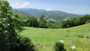 A rural landscape with a grassy field, trees, and distant mountains. - Ca Bastiana (Sevares)