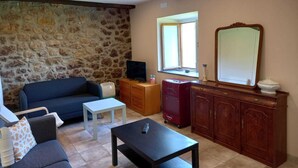 A living room with a stone wall, a blue sofa, a white table, a red heater, and a wooden cabinet with a mirror. - Ca Bastiana (Sevares)