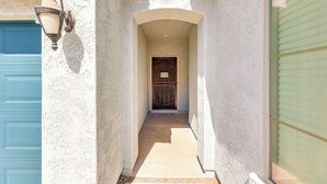 A narrow pathway leading to a door with a metal gate, flanked by a light-colored textured wall and a blue door on the left. - Near Parks & Golf: Maricopa Home w/ Covered Patio! (Maricopa)