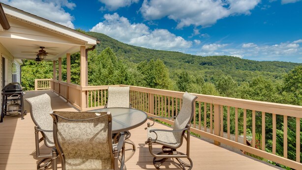 Une terrasse extérieure couverte, dotée d’une table et de chaises, qui offre une vue sur une colline boisée.