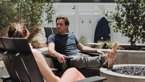 Two people sitting on outdoor chairs near a fire pit, with a building and trees in the background. - Manresa Surf House 1 bed upstairs unit #4 (La Selva Beach)