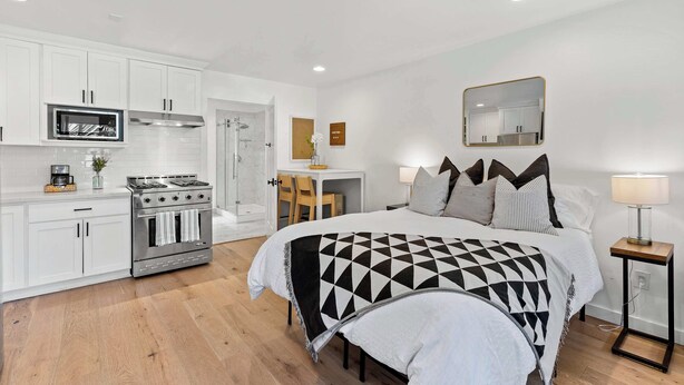 A modern bedroom with a large bed, bedside tables, a desk, and a kitchenette.