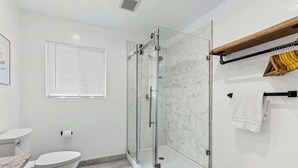 A bathroom with a glass-enclosed shower, a toilet, a sink, and a towel rack.