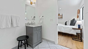A modern bathroom with a vanity, mirror, and a bed in the adjacent room. - Manresa Surf House 1 bedroom Sleeps 4 unit #2 (La Selva Beach)