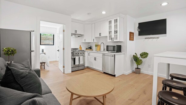 A modern kitchen with white cabinets, stainless steel appliances, and a flat-screen TV mounted above the counter. - Manresa Surf House 1 bedroom Sleeps 4 unit #2 (La Selva Beach)