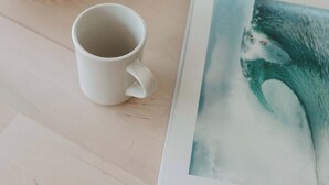 Uma caneca branca sobre uma mesa com um jogo americano de palha e uma planta em vaso.