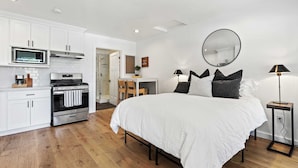 Quarto com uma cama grande, mesa de cabeceira, espelho e vista para a cozinha.