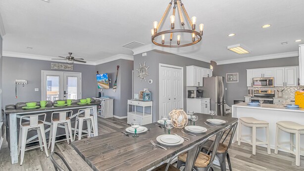 A modern kitchen with a wooden dining table, white bar stools, and a built-in island with seating. - Beautiful 5BR Beach House Ocean Lakes with Ocean and Lake Views (Myrtle Beach)