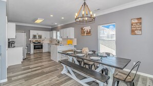 A spacious kitchen with white cabinets, a central island, and a dining area with a wooden table and benches. - Beautiful 5BR Beach House Ocean Lakes with Ocean and Lake Views (Myrtle Beach)