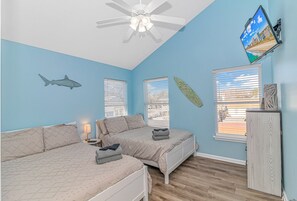 Two beds with white headboards and beige bedspreads, a flat-screen TV, and a ceiling fan.