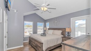 A bedroom with a bed, a ceiling fan, a TV mounted on the wall, and a window with blinds. - Beautiful 5BR Beach House Ocean Lakes with Ocean and Lake Views (Myrtle Beach)