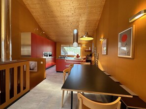 Una cocina moderna con armarios de madera, un comedor con una mesa larga y sillas, y vista al exterior por una ventana.