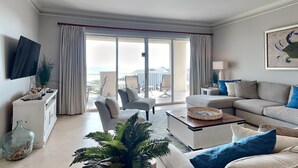A spacious living room with a sofa, armchairs, a coffee table, and a television. There is a sliding glass door leading to an outdoor area with chairs and a table. - San Remo by Southern Vacation Rentals (Santa Rosa Beach)