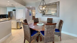A dining area with a round table and wicker chairs, a chandelier, and a large mirror on the wall. - San Remo by Southern Vacation Rentals (Santa Rosa Beach)