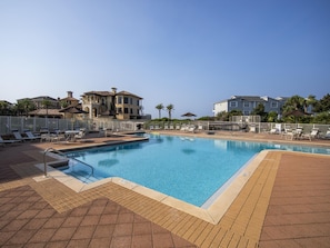 A swimming pool with lounge chairs and umbrellas, surrounded by a fence.