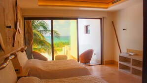 Ein Schlafzimmer mit einem großen Bett, einem Sessel und Meerblick durch eine Schiebetür.