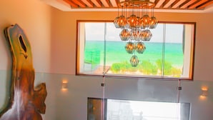Ein modernes Interieur mit einem großen Fenster mit Blick auf einen Strand, einer einzigartigen Holzskulptur und einem modernen Kronleuchter.