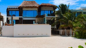 Ein modernes Resort mit einem reetgedeckten Gebäude, Palmen und einem Sandstrand.