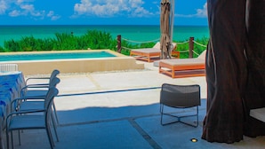 Ein Poolbereich mit Liegestühlen, einem Tisch und einem Sonnenschirm mit Blick auf das klare, blaue Meer.