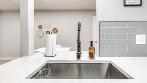 A kitchen with a white countertop, stainless steel sink, and a modern faucet. - "The Cozy Cabana" in Paseo (Oklahoma City)