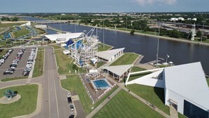 An aerial view of a waterfront area with a large white building, a blue water slide, and a parking lot. - "The Cozy Cabana" in Paseo (Oklahoma City)