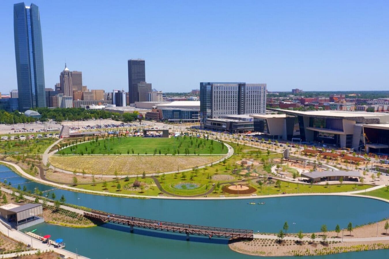 Eine Stadtansicht mit modernen Gebäuden, einem zentralen Park mit kreisförmigem Design und einem Fluss.